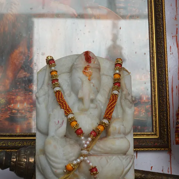Hanuman ji murti garlanded in white and silver instead of marigolds, with the marble Ganesha on the altar and a gold-framed picture on the white wall.