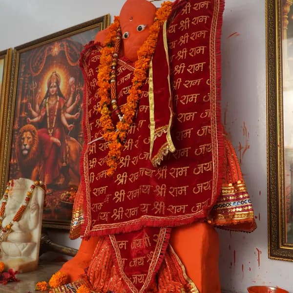 Hanuman ji facing forward in saffron sindoor, marigolds piled at the neck, red Jai Shri Ram cloth over a sequined skirt, Durga on her lion and the marble Ganesha at his side.