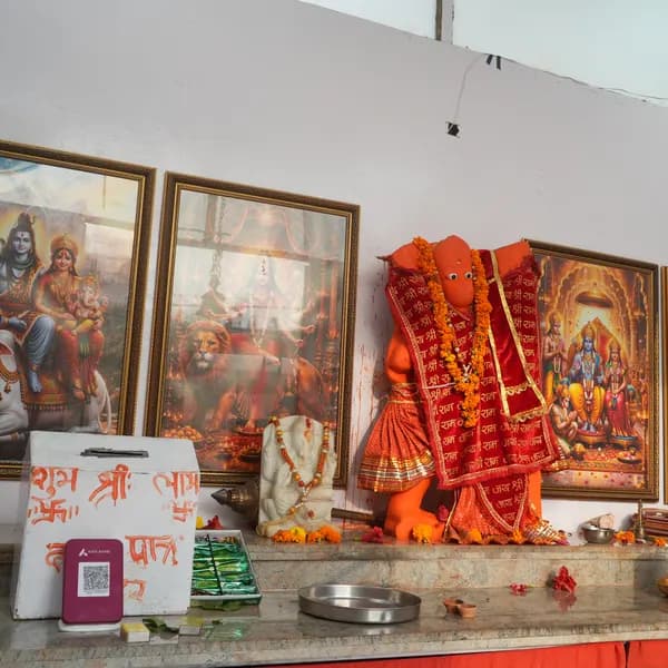 High view of the altar with Hanuman ji, the marble Ganesha, and a white donation box with a purple QR stand, three gold-framed pictures along the wall.