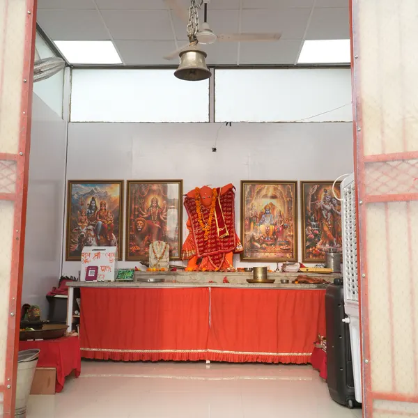 Looking through the orange doorway into the shrine room, the full red-draped altar, four framed deities, a brass bell, and a white tiled floor.