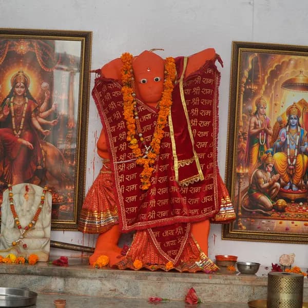 Hanuman ji between framed Durga and Ram Darbar, marble Ganesha at bottom left, marigold petals and a red rose on the grey marble ledge.