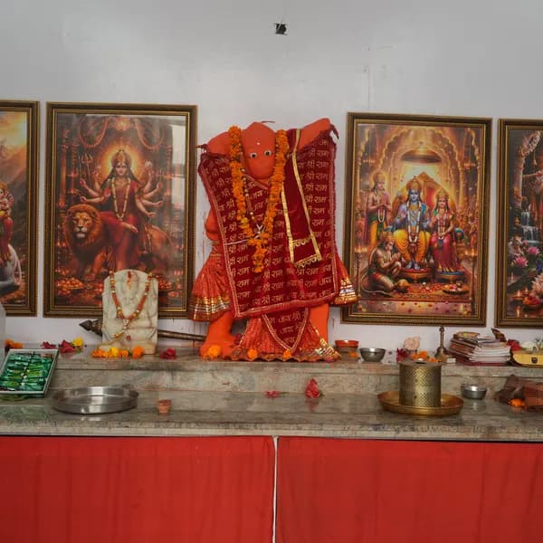 Central altar with Hanuman ji in red and saffron, Durga and Ram Darbar in gold frames, diyas, a thali, and a red cloth covering the base.