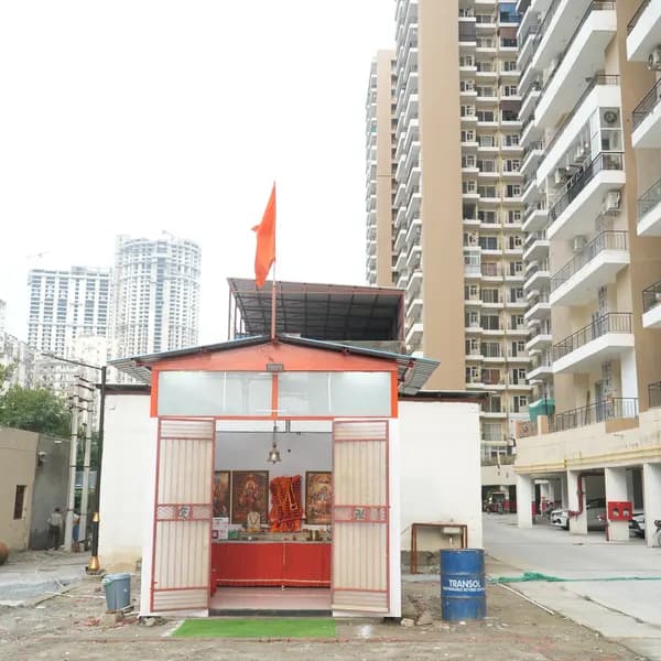 White shrine with red trim and open metal gates, saffron flag on the roof, the red altar visible inside, high-rises of Crystal Homes behind.