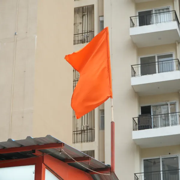 Saffron dhwaja flying from the corrugated roof, apartment balconies stacked behind it.