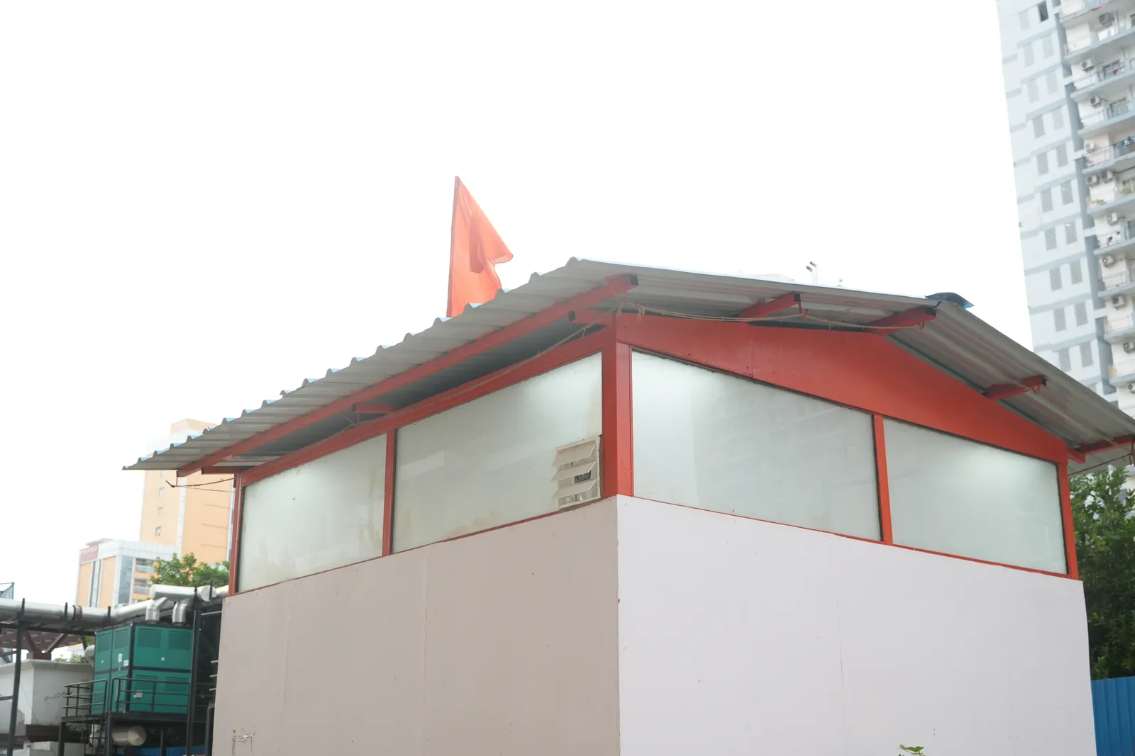 Small white shrine with a saffron flag on its roof, Noida apartment towers behind